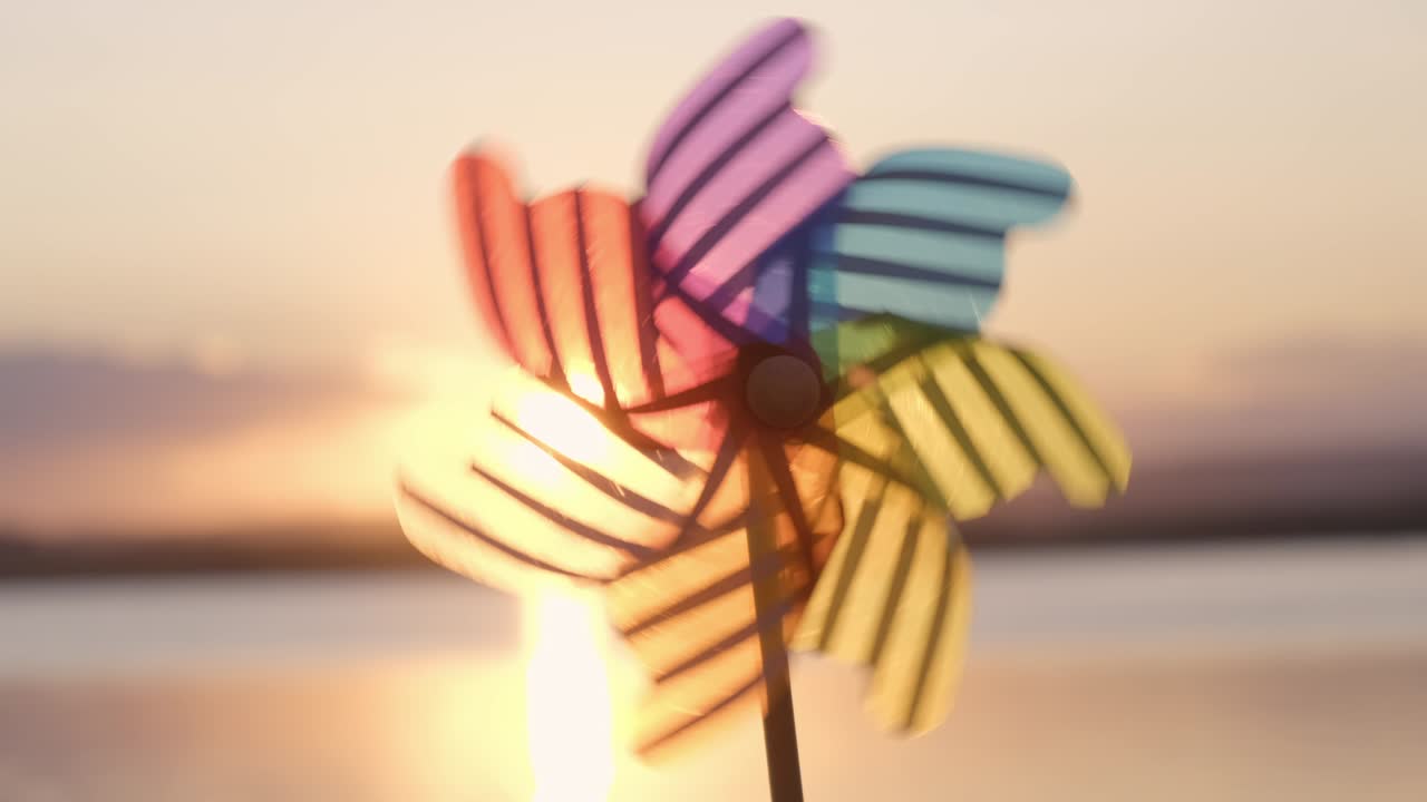 Rotate colored plastic pinwheel with a blowing wind stands on sand by the sea against the smooth surface of the sea and a bright pink sunset. Toy mill on the beach. Large disk of the sun. Copyspace