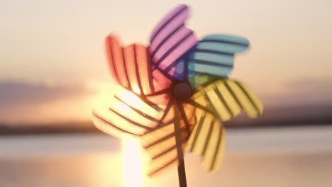 rotate colored plastic pinwheel with a blowing wind stands on sand by the sea against the smooth surface of the sea and a bright pink sunset. toy mill on the beach. large disk of the sun. copyspace