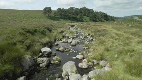 a picturesque view of a small stream meandering through an expansive green landscape in the wicklow mountains, ireland - drone flying forward