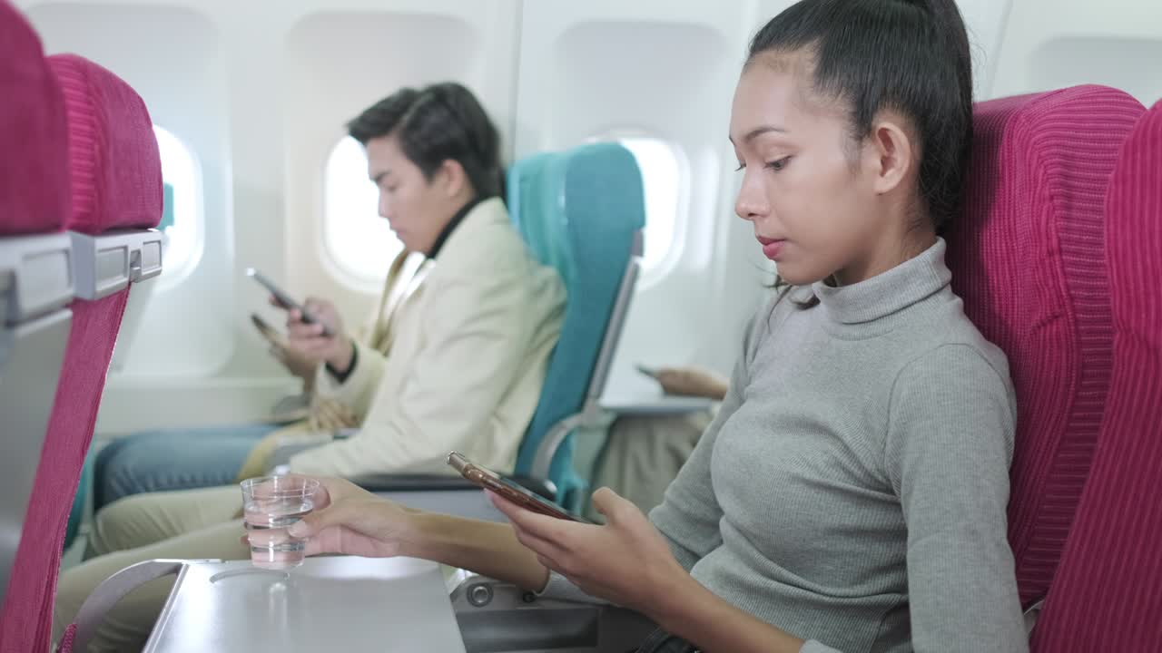 アジアの女性乗客飛行中に水を飲み離陸前にスマートフォンでソーシャルネットワークを見るエコノミー座席で飛行機を飛ぶ初めての飛行機で興奮を感じる - ライブドアニュース