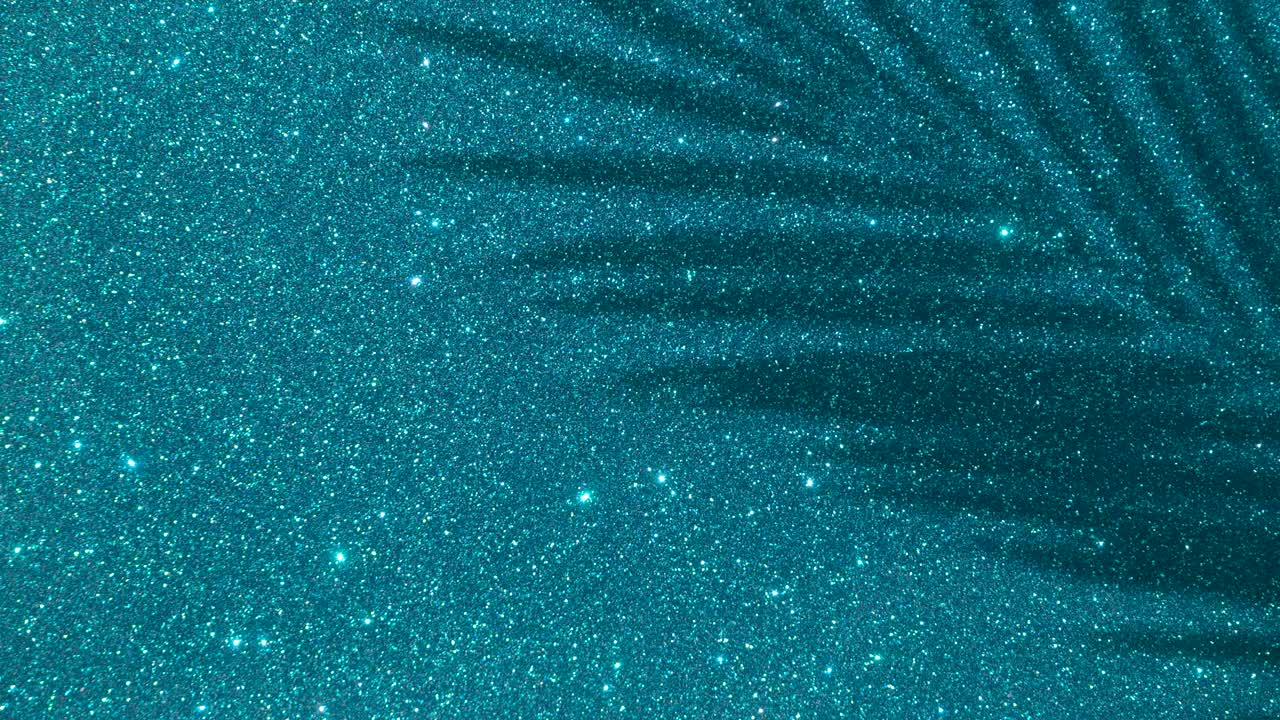 Shadows from a palm tree on a blue glitter sparkling shining background. Minimal art, glamor, vacation, summer, party concept.
