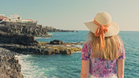 Rear-view,-woman-in-cute-hat-watching-ocean-waves-hitting-sharp-cliffs