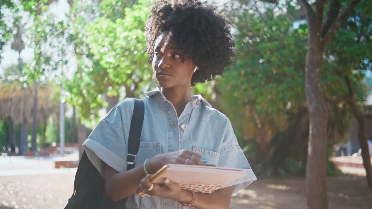 Adolescente che cammina per strada in una giornata di sole tenendo dei libri, primo piano. Donna che passeggia.