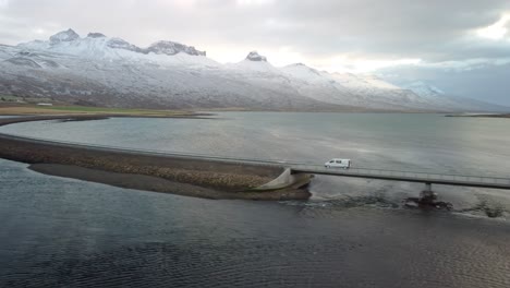 una foto de un avión no tripulado de un hermoso paisaje en islandia, de un coche conduciendo por una carretera a través del mar y las montañas en el fondo