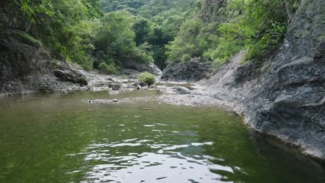 drone flying at low altitude over calm water of river in forest, las yayitas, bani in dominican republic