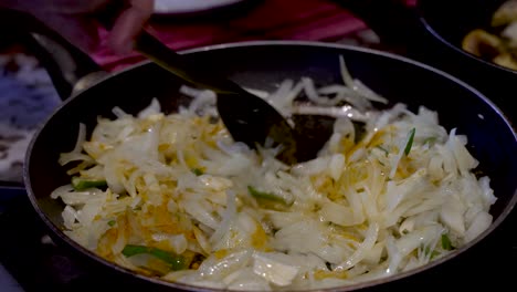 a close up shot of the hand of a chef carefully stirring freshly chopped raw onions and green chillies in a hot non-stick frying pan with a spatula