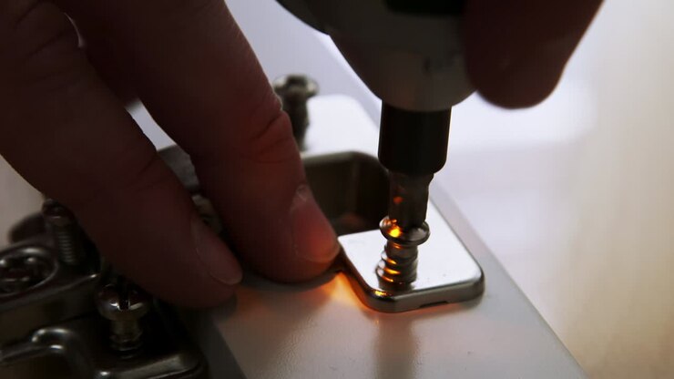 Caucasian hands put a hinge into a socket of a glass cabinet