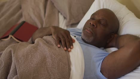 Tired-african-american-senior-lying-on-back-asleep-in-bed-with-book-on-bed