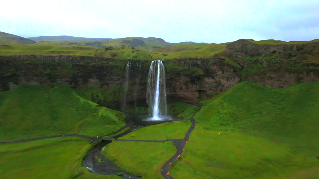 This drone video beautifully captures the striking contrast between the roaring waterfall and the tranquil landscape of Seljalandsfoss.