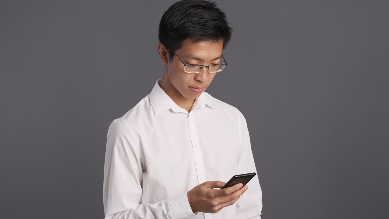 Pensive Asian man using smartphone.