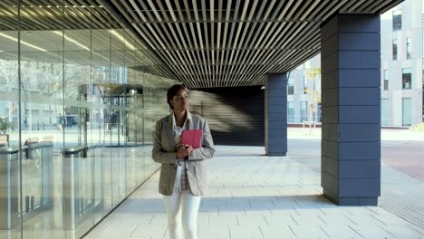 business woman holding digital tablet while walking outside office building in financial district.