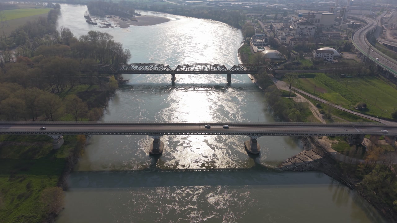 Drone aerial view of road and railway bridges crossing Po River in Italy. Strategic transport infrastructure connecting regions with highway and train traffic.
