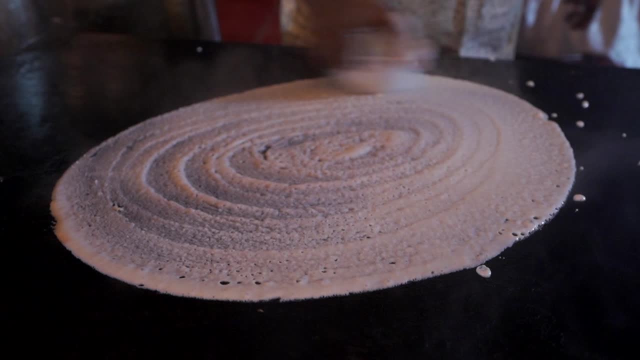 indian street food vender making dosa on hot pan