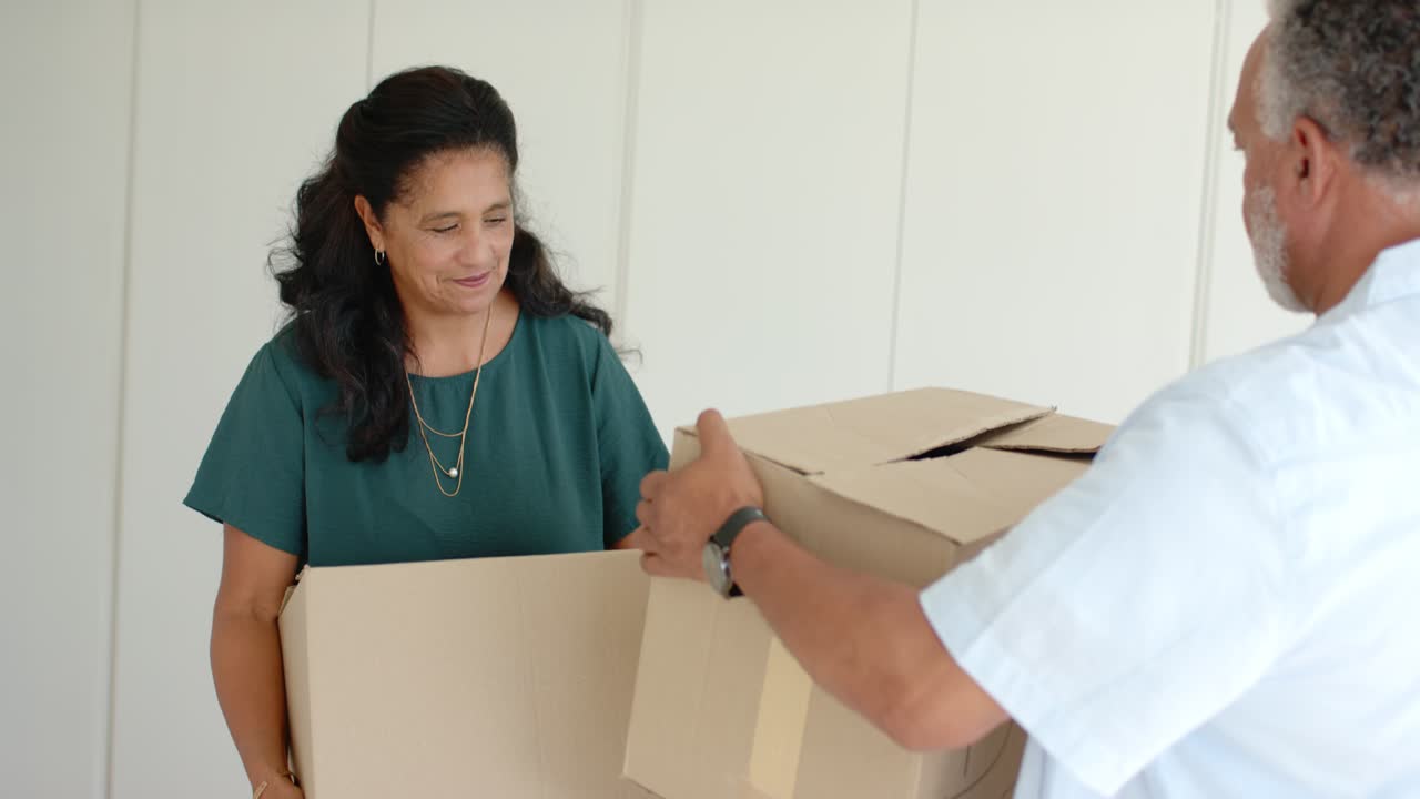 African American couple packing cardboard boxes on white cloth at home, lifting boxes for move