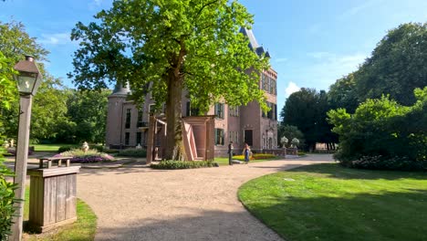 a steady camera glides along a curved garden path toward a historic castle, surrounded by lush greenery and bright daylight in lisse, netherlands