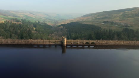 Aerial-view-passing-Scar-house-reservoir-landmark-flying-out-towards-vibrant-Yorkshire-valley-countryside