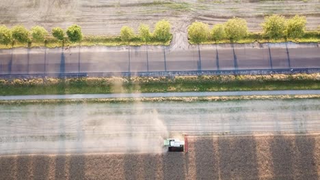 Tractor-combine-harvesting-crops-next-to-avenue-with-trees-casting-shadows-on-the-road