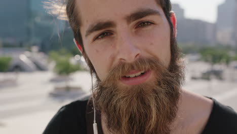 slow motion portrait of handsome young hipster man student with beard listening to music wearing earphones looking serious at camera in urban background