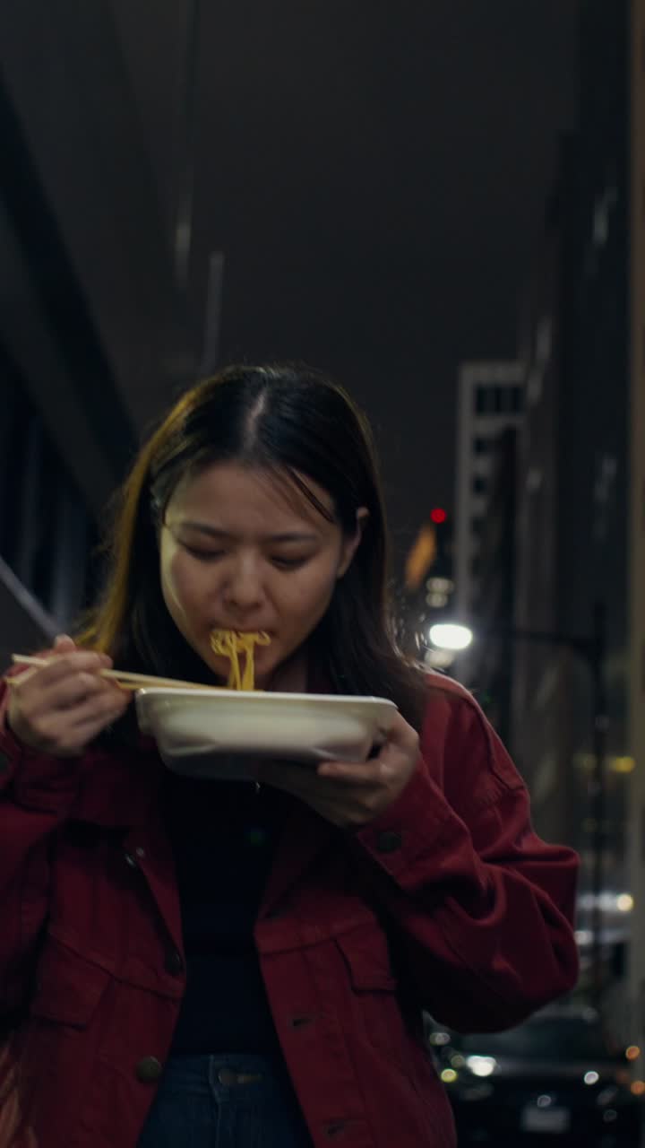 Woman Eating Noodles on a City Street at Night