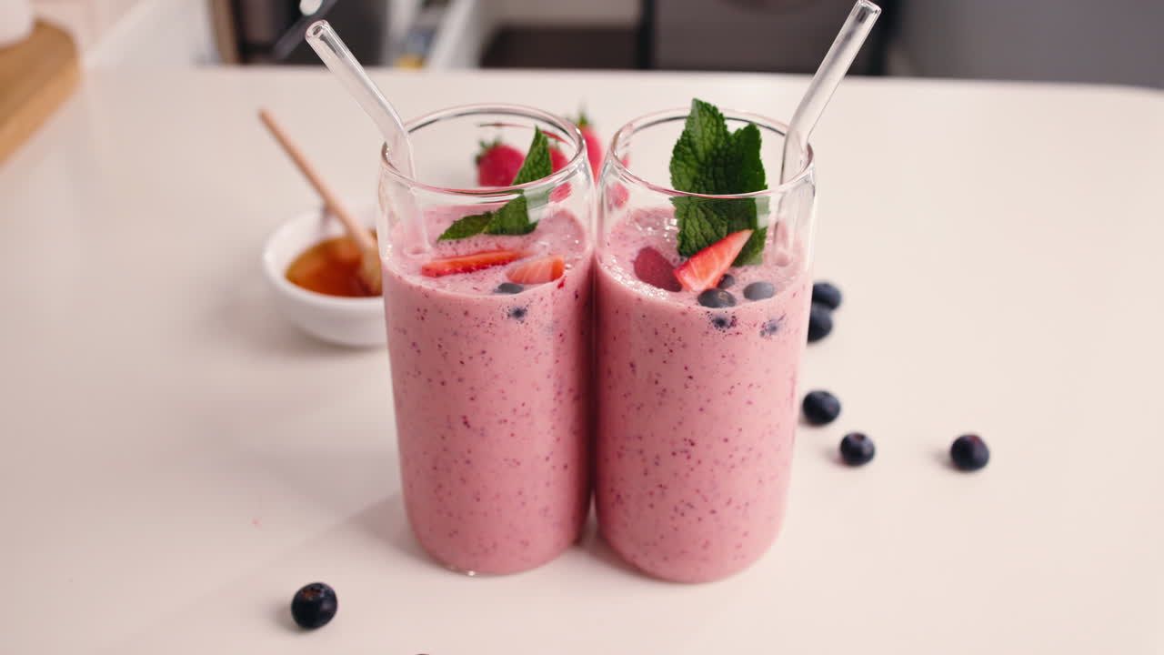 Dos batidos de frutos rojos adornados con fresas frescas, arándanos y menta