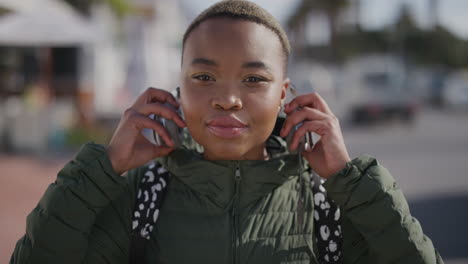 retrato de una joven mujer afroamericana que se pone auriculares escuchando música bailando feliz disfrutando de unas cálidas y vibrantes vacaciones de verano en el fondo de la playa urbana