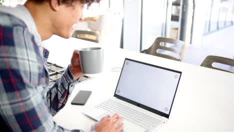 holding coffee mug, man using laptop and smartphone on kitchen counter
