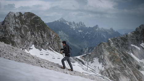 Hiker-climbing-up-a-hill-on-mountain-Kanin-with-a-beautiful-view-of-other-mountains-in-the-background,-clouds-covering-the-sky