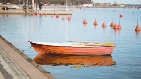 small wooden rowboat with oars floating on the water while anchored in the dock