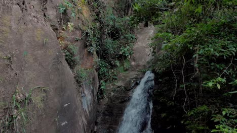 Movimiento-Panorámico-Lento-Hacia-Abajo-Que-Muestra-Una-Cascada-Que-Emerge-Del-Espeso-Bosque-Tropical-De-Montaña-De-Río-De-Janeiro-Hasta-Desembocar-En-Un-Estanque