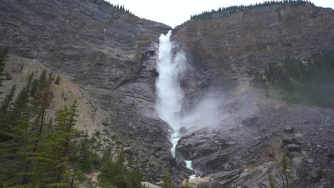 large waterfall revealed through trees and flowing down a mountain creating rapids as it continues to flow down the mountain