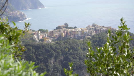 slow motion slide reveal of corniglia in cinque terre, italy from behind bushes on blue path trail