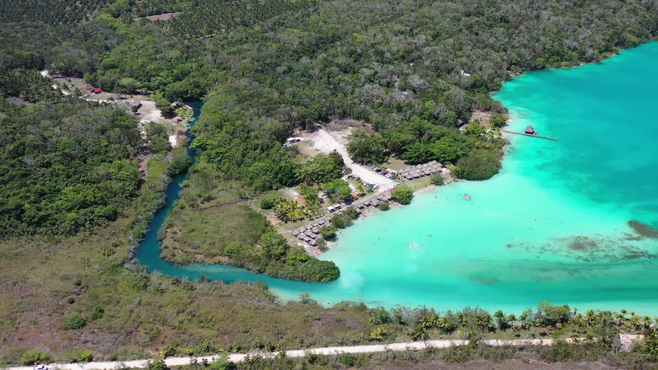 Drone aerial of Bacalar Lagoon, Mexico showing vibrant turquoise water winding through lush jungle and wetlands. Stunning natural landscape highlighting the famous “Lagoon of Seven Colors.”