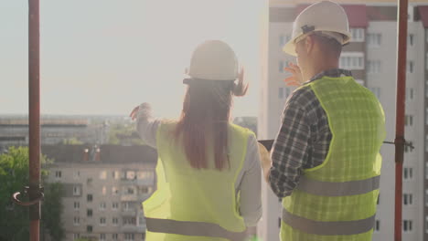 Pareja-De-Ingenieros-O-Técnicos,-Hombre-Y-Mujer-Con-Casco-De-Seguridad,-Sosteniendo-Un-Teléfono-De-Radio-Móvil,-Planificando-El-Plan-De-Construcción-Para-Saludar-El-Inicio-Del-Proyecto-En-El-Concepto-De-La-Industria-De-La-Construcción-En-El-Sitio-De-Construcción.