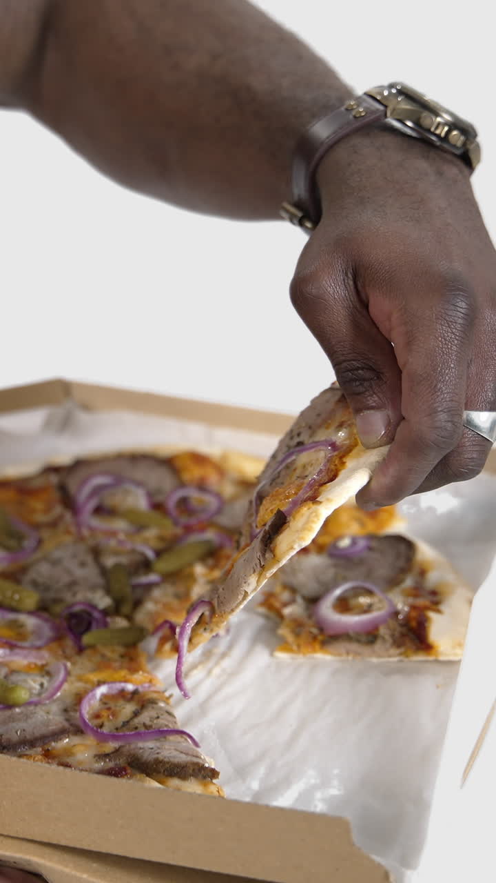 Delicious pizza in black man's hands. African man holds a box with delivered pizza and trying to eat some slice. Unhealthy food. Close-up. Slow motion. Vertical video