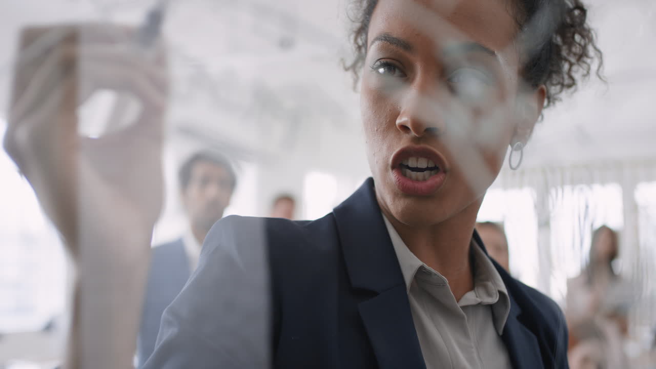 mujer de negocios de raza mixta líder de equipo escribiendo en pizarra de vidrio entrenando colegas compartiendo ideas de resolución de problemas en la presentación de seminarios corporativos