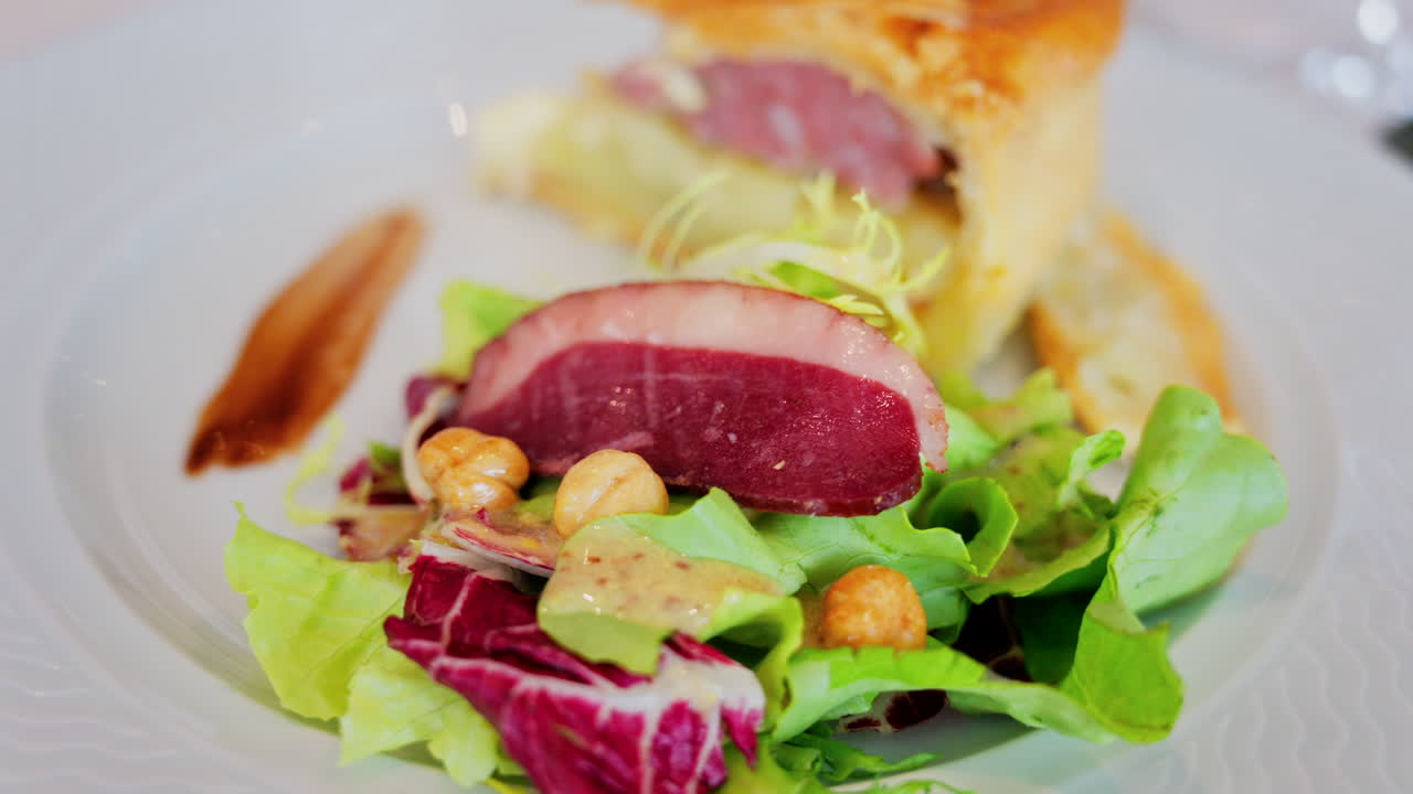 Close up of a slice of quiche featuring with a side salad and a slice of cured meat on a white plate at a restaurant