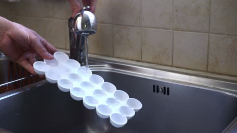 hombre caucásico llenando una bandeja de cubitos de hielo con agua en casa