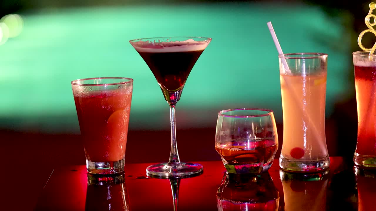 Multiple hands clink assorted cocktails on glossy red bar table, vibrant lighting, shallow depth