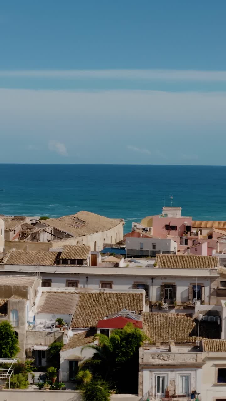 Vertical drone shot flying sideways above buildings in the island of Ortigia, Syracuse. Medieval old town buildings from above with Mediterranean sea in the background. UNESCO world heritage site.