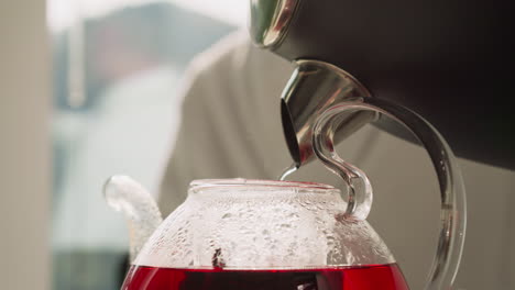 pouring boiling water from kettle into teapot closeup. brewing hibiscus tea enjoying aromatic steam of plant in kitchen. concept of relaxation