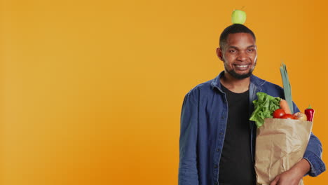 joven adulto tratando de mantener el equilibrio con una manzana en la cabeza en el estudio