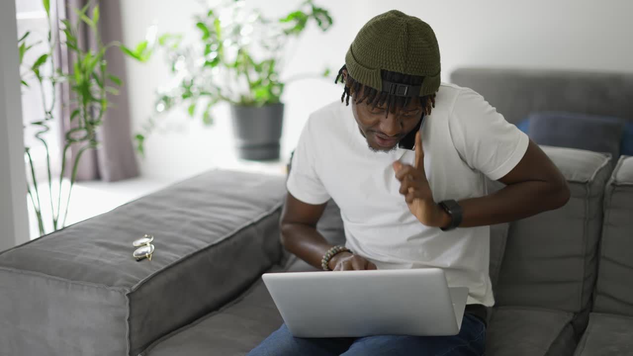 African Man using smartphone while using laptop on sofa