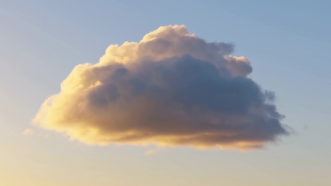 A large fluffy cloud floats near the center of the frame in a clear blue sky, warmed by soft golden sunlight from the lower left, creating a calm and spacious
