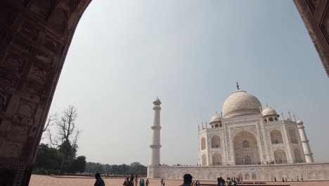 the taj mahal framed from an arch gate. visitors walk outdoors. agra, india.