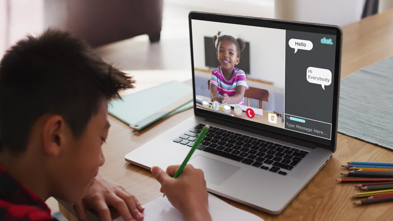 Schoolboy using laptop for online lesson at home, with girl talking and web chat on screen