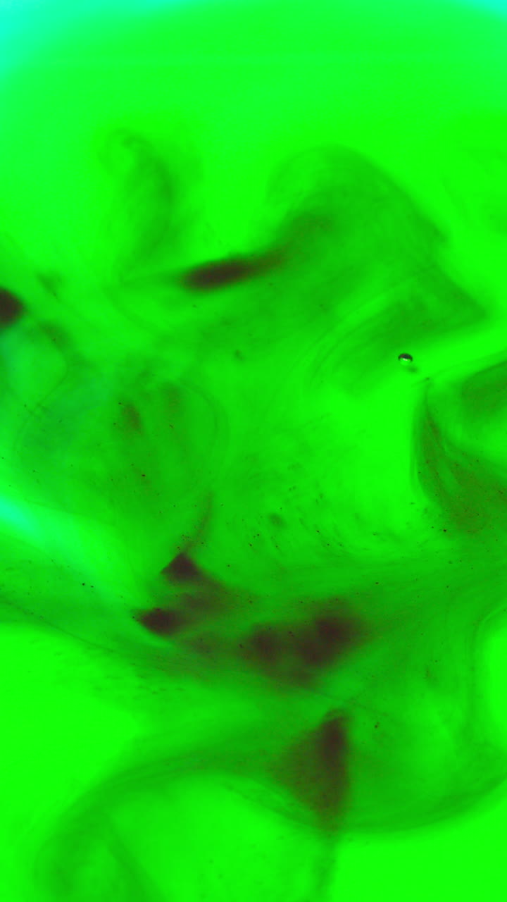 toma de video vertical de pintura o tinte negro y verde caído en el agua contra un fondo blanco para crear un fondo de humo colorido giratorio