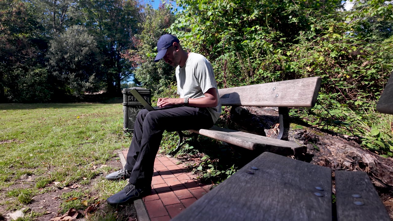 Freelancer working outdoor with laptop sitting on park bench enjoying good weather