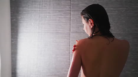 woman takes care of skin with scrub in shower cabin closeup. graceful lady applies peeling natural cosmetic product on shoulder in bathroom