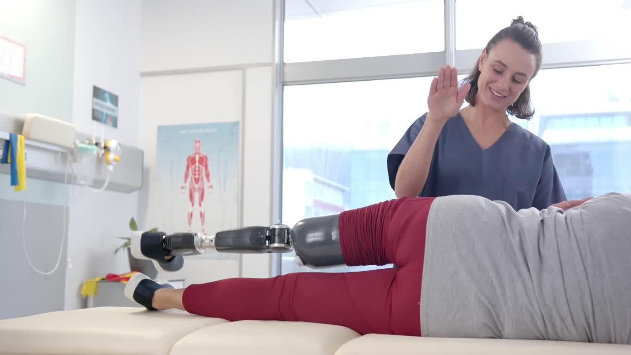 Caucasian female physiotherapist stretching prosthetic leg of female patient at rehab center