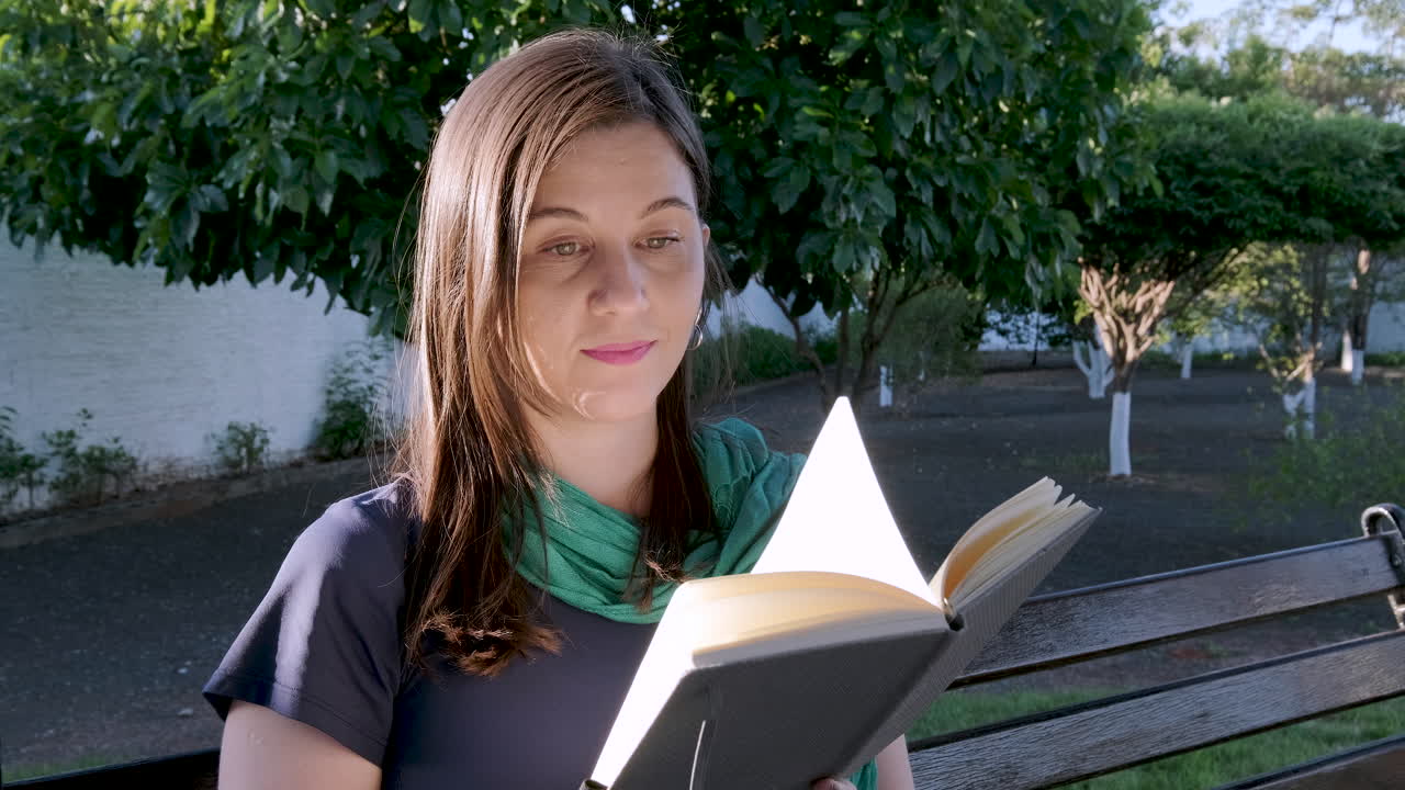 joven estudiante caucásica mujer gira lentamente la página del libro al aire libre